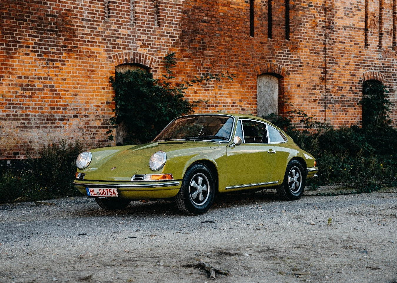 1969 Porsche 911T olive green parked in front of a brick wall