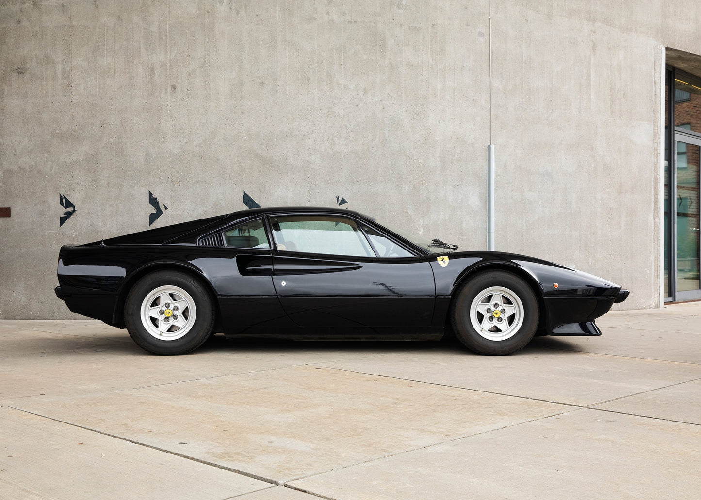 Black 1977 Ferrari 308 GTB dry sump parked in front of a concrete wall.