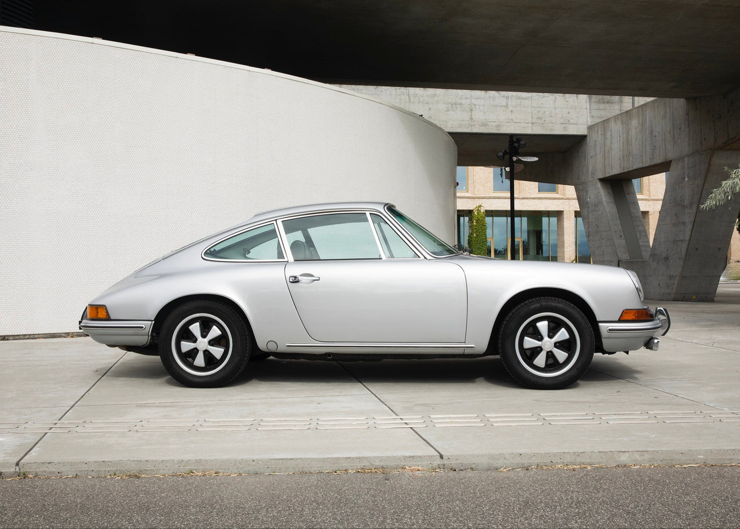 Silver 1969 Porsche 911T parked on a concrete surface with a modern architectural background